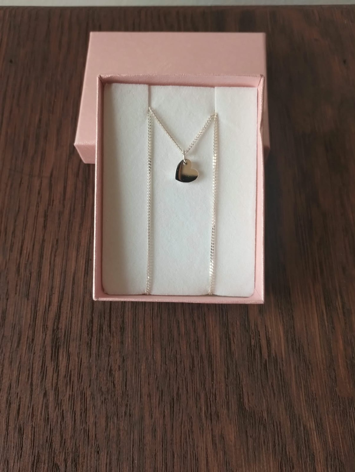 Dije de corazón liso con cadena en una caja rosa