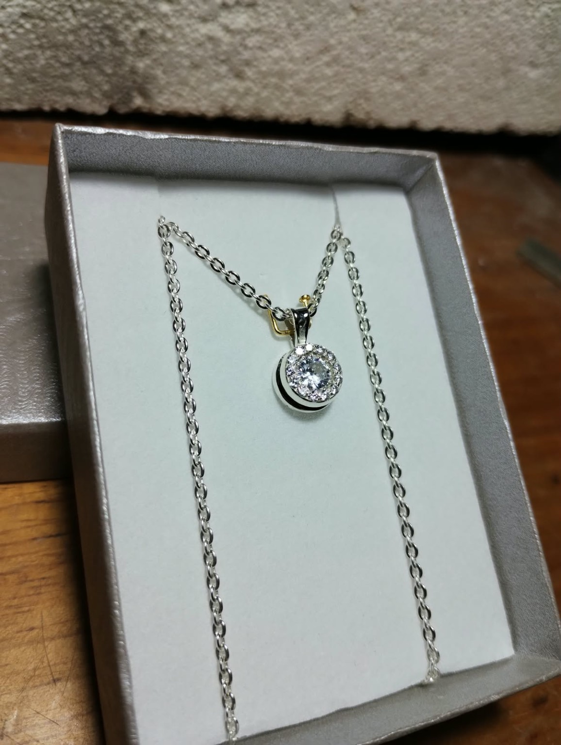Dije circular con una piedra central rodeada de piedras pequeñas, presentado con su cadena