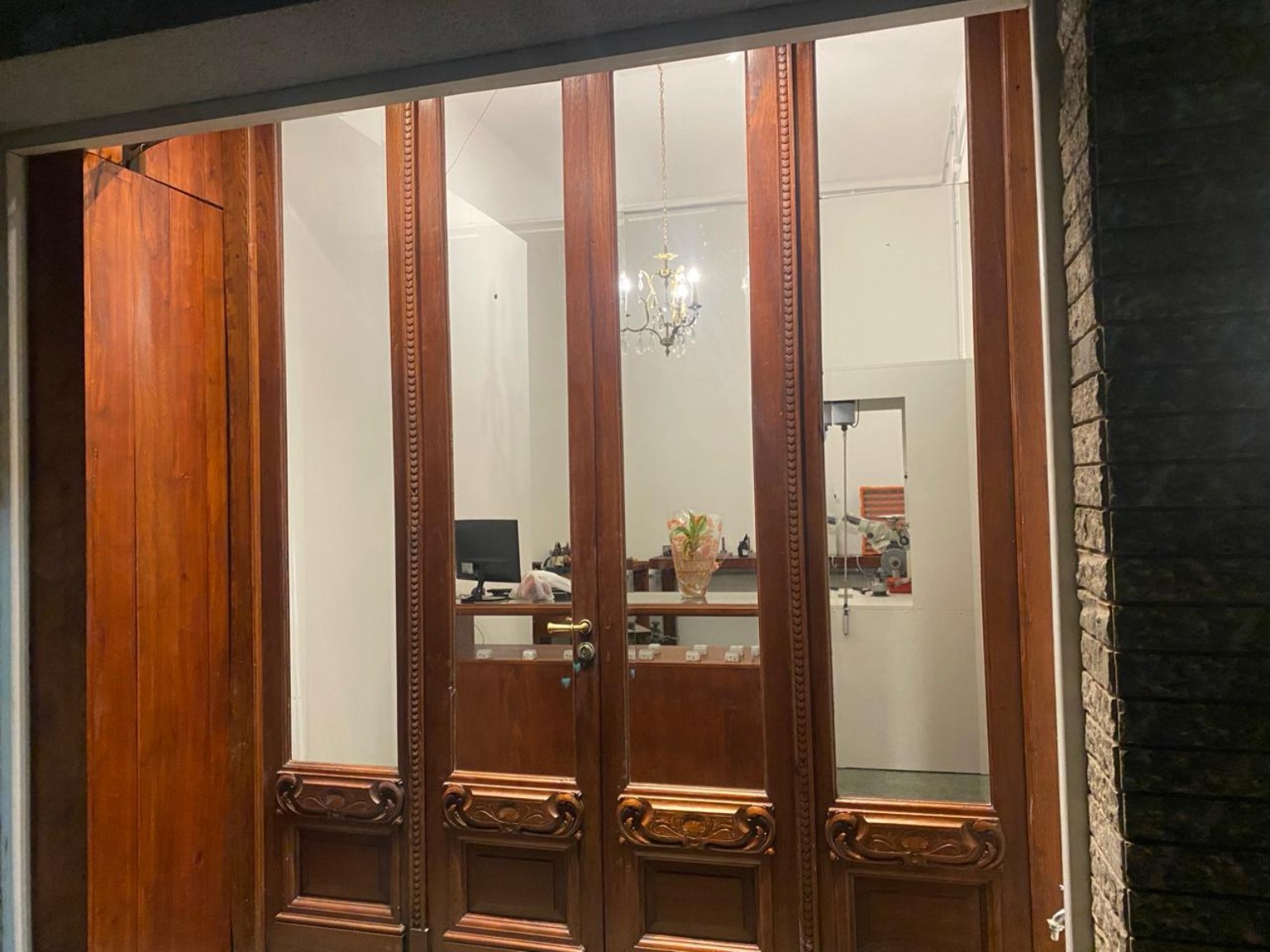 Entrada de cedro de Joyas Taller iluminada de noche, con el taller visible detrás del vidrio